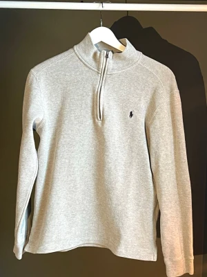 Grå halvzip från Ralph Lauren - Snygg ljusgrå tröja från Ralph Lauren med halv dragkedja och hög krage. Klassisk broderad logga på bröstet. Tillverkad i mjukt bomullsmaterial och har långa ärmar. Perfekt för en clean och stilren look. Storlek är 170 i barn, men måtten stämmer överens med en storlek XS / S Köpt från Ralph Lauren, använd fåtal gånger 🫧