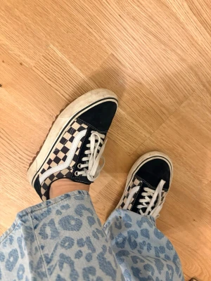 Vans Old Skool Checkerboard sneakers - Säljer ett par klassiska Vans Old Skool sneakers med svart och vit checkerboard-mönster på sidan, svarta detaljer i mocka och vita snören. Ikonisk vit sula och den typiska Vans-vågen på sidan. Perfekta för en streetwear-look. MTE modellen för höst/vinter storlek 37. Se bilder för skick 