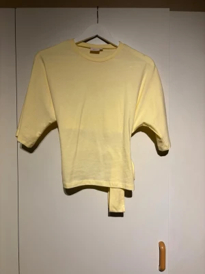 Gul croppad topp med knytband - Snygg ljusgul croppad topp med korta ärmar och knytband i midjan som ger en unik look. Kommer inte till användning 