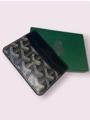 Svart  korthållare i läder - Snygg svart korthållare med ett klassiskt mönster i vitt och brunt. Tillverkad i exklusivt läder och har flera fack för kort. Kommer i original grön ask. Perfekt för dig som vill ha något stilrent och lyxigt i fickan. Priset kan diskuteras vid snabb affär! Kolla gärna igenom min profil för annat!