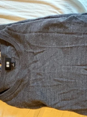 Mörkgrå stickad tröja Uniqlo - Mörkgrå stickad tröja från Uniqlo i klassisk modell med rund halsringning och ribbade muddar. Tillverkad i mjukt material som passar perfekt för lager på lager. Enkel och stilren design som funkar till det mesta. 