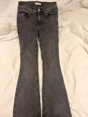 Grå bootcut jeans från Ginatricoot - Snygga grå bootcut jeans från Perfect Jeans med klassisk femficksmodell och låg midja. Jeansen har en lätt tvättad look och är tillverkade i stretchigt denimtyg för extra komfort. Perfekta för dig som gillar en avslappnad men trendig stil.