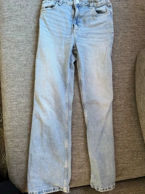 Ljusblå raka jeans i denim - Säljer ett par ljusblå jeans med rak passform och klassisk femficksdesign. Jeansen har hög midja och är tillverkade i ett mjukt denimtyg. Perfekta för en avslappnad och trendig look.
