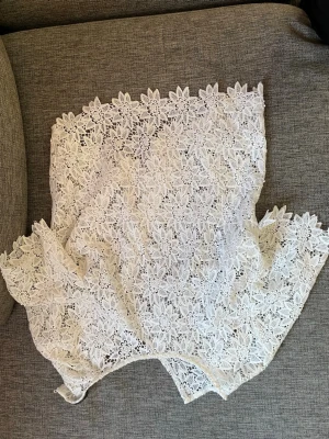 Vit spetsblus med blommönster - Supersöt vit blus i spets med blommigt mönster. Blusen är ärmlös och har en rak passform. Perfekt för dig som gillar romantiska detaljer och vill ha en luftig topp till sommaren. Ingen synlig logga eller märke.
