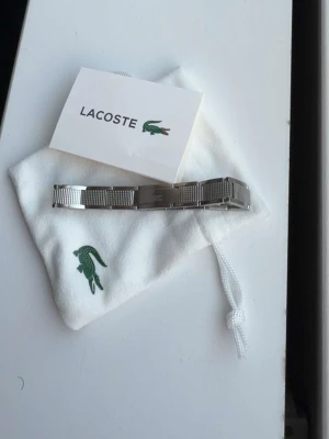 Lacoste armband  - Ett fint Lacoste armband, som kan göras mindre. Den är i fint skick och säljer den billigt pågrund av att jag vill få sålt den snabbt. Hör gärna av dig om du är intresserad!!