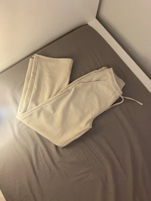 Beige mjukisbyxor med dragsko - Säljer ett par beige mjukisbyxor med resår i midjan och dragsko för skön passform. Byxorna har raka ben och sidofickor. Perfekta för chill dagar hemma eller när du vill vara bekväm. Materialet känns mjukt och följsamt.