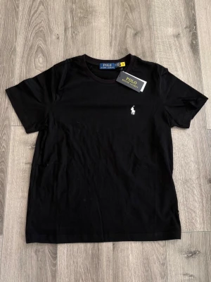 🖤Svart t-shirt från Polo Ralph Lauren🖤 - Klassisk svart t-shirt från Polo Ralph Lauren med den ikoniska vita broderade loggan på bröstet. T-shirten har rund halsringning och korta ärmar. Tillverkad i mjuk bomull för en skön känsla och enkel stil. Tar emot bud.
