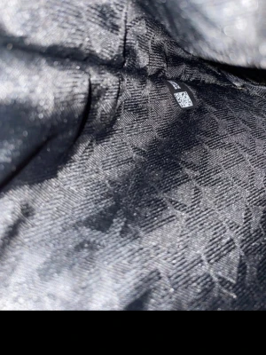  Michael Kors Tore travel bag - Snygg svart handväska från Michael Kors i tåligt saffiano-läder. Väskan har guldfärgade detaljer, logotyp framtill och justerbara axelband. Insidan har ett diskret mönster med MK-loggor. Perfekt för dig som vill ha en stilren och rymlig väska. Helt nyskick. Äkta med stämpel. 1050kr med frakt. 