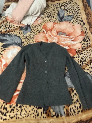 Mörkgrå ribbstickad kofta - Mörkgrå ribbstickad kofta med v-ringning och knäppning framtill. Långa ärmar och figurnära passform ger en stilren look. Perfekt att slänga över en t-shirt eller topp för extra värme. Helt oanvänd. 