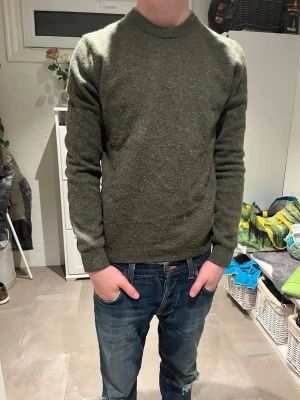 Grön stickad tröja These Glory Days - Mörkgrön stickad tröja från These Glory Days med rund halsringning och ribbade muddar vid ärmslut och nederkant. Tröjan har en klassisk, rak passform och är tillverkad i ett mjukt, värmande material som passar perfekt till jeans.