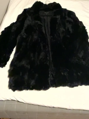 Svart fuskpälsjacka från Willys - Säljer en svart fuskpälsjacka från Willys med klassisk krage och hel dragkedja framtill. Jackan har en fluffig och mjuk känsla, perfekt för kalla dagar. Passar dig som vill ha en stilren och trendig look under vintern.