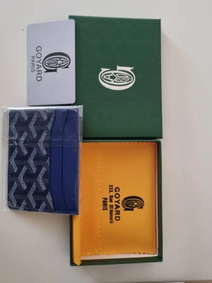 Blå korthållare från G4yard - Snygg blå korthållare från G4yard med det klassiska vita mönstret och flera kortfack. Tillverkad i canvas och läder, levereras med original grön ask och gul putsduk. Perfekt för dig som vill ha en exklusiv och stilren accessoar.