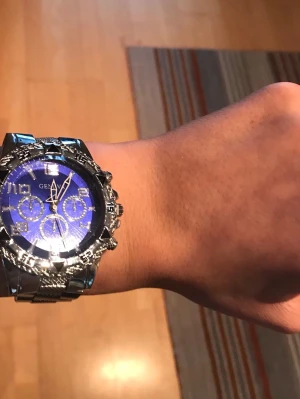 Blå klocka  - Snygg klocka från Geneva med blå urtavla och silverfärgat armband i metall. Klockan har flera dekorativa subdials och markerade siffror, samt en robust boett med detaljer runt urtavlan. Perfekt accessoar för dig som vill sticka ut.