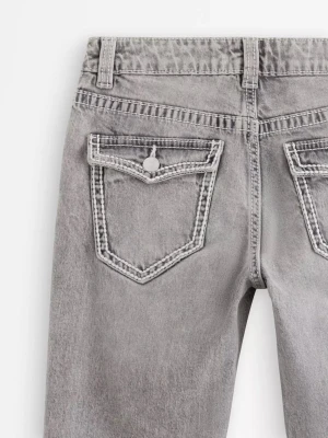 Grå bootcut jeans med fickdetaljer - Säljer ett par grå bootcut jeans med markerade sömmar och fina detaljer. passformen är rak med lätt utsvängda ben. de är knappt använda men är lite slitna längst ned vid ena byxbenet, annars inga skador
