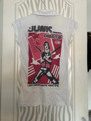 Vit t-shirt med tryck och krage - Vit t-shirt från junk shop med coolt rött och svart pirattryck både fram och bak. T-shirten har korta ärmar, klassisk krage och knappar framtill. Materialet är tunn bomull, perfekt för en avslappnad och edgy stil. 