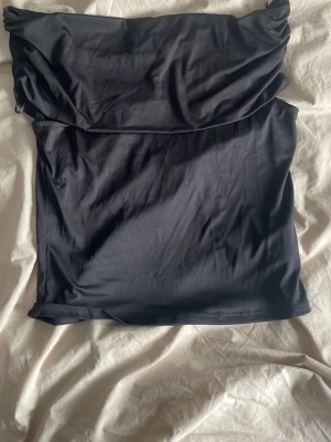 Svart off shoulder topp - Snygg svart axelbandslös tubtopp med enkel och stilren design. Toppen har en bandeauformad överdel och är tillverkad i ett mjukt, stretchigt material som sitter bekvämt mot kroppen. Perfekt att matcha med jeans eller kjol för en trendig look.