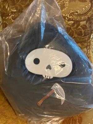 Mjukisdjur dödskalle med lie - Säljer ett svart mjukisdjur format som en dödskalle med vit ansikte och svart huva. På magen finns en liten lie med brunt handtag och silverfärgat blad. Perfekt som dekoration eller present till någon som gillar unika gosedjur.