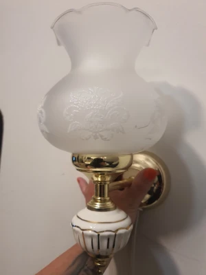 Vägglampa i mässing och frostat glas - Säljer en klassisk vägglampa med frostat glas och blommönster. Lampan har detaljer i mässing och vit keramik med guldfärgade ränder. Perfekt för dig som gillar vintage eller vill ha en elegant touch i rummet. Monteras på väggen och har sladd för eluttag.