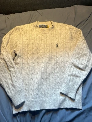 Ralph lauren kabelstickad tröja  - Det är som sagt en kabelstickad tröja från Ralph Lauren. Den är grå men ett svart Ralph lauren emblem. Det är i bra skick skulle säga 8-9/10 Den är egentligen i Stolek S men den passar garanterat Xs eller Xxs. Jag är lite mellan Stolek S och xs men det är pågränsen till förliten.