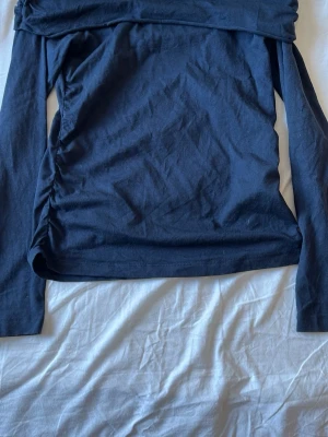 Mörkblå offshoulder topp - Trendig mörkblå offshoulder topp med långa ärmar. Toppen har en bred kant upptill som ger en snygg och stilren look. Perfekt för dig som vill ha en enkel men ändå unik topp i garderoben. Använd fåtal gånger då den inte passar mig.