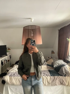 Olivgrön bomberjacka med dragkedja - Snygg olivgrön bomberjacka med klassisk passform och ribbade muddar vid ärmslut och krage. Jackan har dragkedja framtill och två fickor på sidorna. 