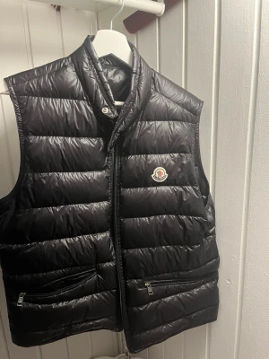 Moncler Gui Väst – Svart - Moncler Gui Väst – Svart 🧥 Modell: Gui Vest 📏 Storlek: 3 (motsvarar ungefär M) 🖤 Färg: Svart 🔄 Skick: 8/10 – använd men i fint skick