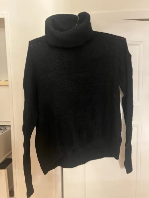 Svart polotröja stickad - Mysig svart stickad polotröja med hög krage och långa ärmar. Tröjan har en enkel, klassisk design och är ribbstickad vid kragen och muddar. Perfekt för kyliga dagar och lätt att matcha med olika outfits.