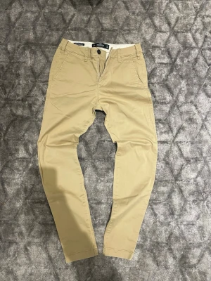 Beige chinos från Hollister - Snygga beige chinos från Hollister med klassisk passform och raka ben. Tillverkade i mjuk bomull som ger en skön känsla hela dagen. Perfekta att matcha med en hoodie eller skjorta för en clean look.