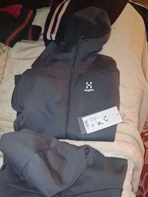 Mörkgrå hoodies från Haglöfs dam  - Snygg mörkgrå hoodie från Haglöfs med dragkedja framtill och klassisk huva. Tillverkad i ett mjukt och funktionellt material som passar perfekt för både chill och aktivitet. Diskret Haglöfs-logga på bröstet och praktiska fickor på sidorna. Enkel och stilren design. Helt Nya haglöfs hoodie för damer Helt Nya oanvända köpta för 1600 men råkade beställa två likadana säljes för 1000 st en medlum och en smal dom.e likadana a 