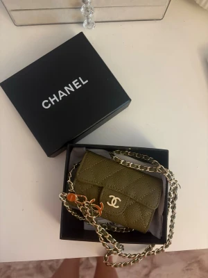 Olivgrön Chanel plånbok med kedja - Snygg olivgrön plånbok från Chanel i quiltat läder med guldfärgad kedja och klassisk CC-logga framtill. Perfekt att bära crossbody eller som accessoar. Kommer i originalask. Finns i alla färger leverans 1-3 veckor 