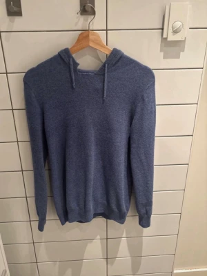 Blå cashmere hoodie - Mysig blå hoodie med huva och dragsko. Tillverkad i mjukt material som känns skönt mot huden. Klassisk modell med långa ärmar och ribbade muddar vid ärmslut och nederkant. Perfekt för en avslappnad och chill stil.