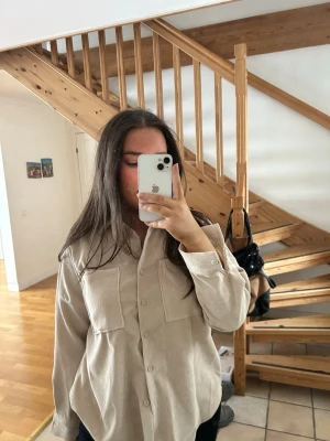 Beige oversized skjortai manchester liknande - Snygg beige overshirt i manchester med två stora bröstfickor och knäppning framtill. Skjortan har en avslappnad passform och långa ärmar, perfekt att styla lager på lager.