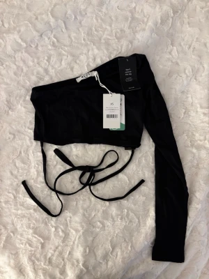 Svart oneshoulder topp NA-KD - Svart oneshoulder topp från NA-KD med lång ärm på ena sidan och knytband i midjan. 