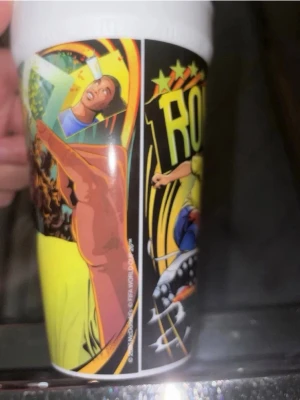 McDonald's FIFA plastmugg - Cool plastmugg från McDonald's med färgglad tecknad design inspirerad av fotboll och FIFA. Motivet visar en spelare i gul tröja och bakgrunden har gröna, gula och svarta detaljer samt McDonald's-logga. Perfekt för samlare eller fotbollsälskare.