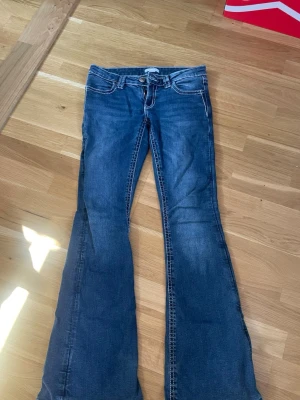 Blå bootcut jeans med broderade fickor - Säljer ett par blå bootcut jeans med snygga broderade detaljer på bakfickorna och kontrastsömmar. Jeansen har låg midja och klassisk femficksmodell. Perfekta för dig som gillar en retro och avslappnad stil.