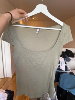 Grön basic topp från Nelly - Enkel och stilren grön topp från Nelly med korta ärmar och rund, djup urringning. Tillverkad i mjuk bomull som känns skön mot huden. Perfekt att matcha med jeans eller kjol för en clean look.