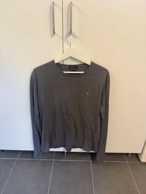 Grå långärmad tröja från GANT - Säljer en stilren grå långärmad tröja från GANT med rund halsringning och liten broderad logga på bröstet. Tröjan är i mjuk bomull och har en klassisk passform som funkar till det mesta. Perfekt basplagg för garderoben!