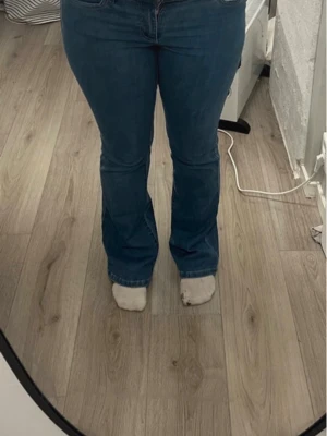 Blå bootcut jeans med hög midja - Säljer ett par blå bootcut jeans med hög midja och klassisk femficksdesign. Jeansen har en snygg tvätt och är tillverkade i ett stretchigt denimtyg som sitter bekvämt. Perfekta för dig som gillar en retroinspirerad look.