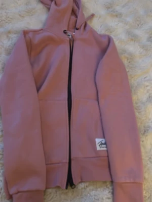 Rosa hoodie från Andy by Frank Dandy - Säljer en rosa hoodie från Andy by Frank Dandy med dragkedja framtill och huva med dragsko. Hoodien har en mjuk insida och ribbade muddar vid ärmslut och nederkant. Perfekt för en avslappnad och trendig stil.