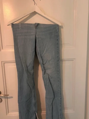 Ljusblå bootcut jeans från Zara - Säljer ett par ljusblå bootcut jeans från Zara med hög midja och klassisk femficksdesign. Jeansen har slitsar nedtill på benen och är tillverkade i stretchigt denimtyg för en bekväm passform. Perfekta för en avslappnad och trendig look.