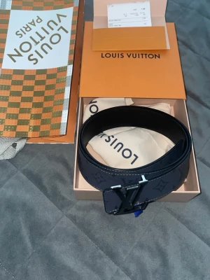 Louis Vuitton bälte - Snyggt svart skärp från Louis Vuitton med klassiskt monogrammönster och stor LV-logga i silver som spänne. Skärpet är tillverkat i skinn och levereras med originalbox, dustbag och kvitto. Den är knappt använd max 1-2 gånger är som helt ny, köpt för 4800kr och är äkta.