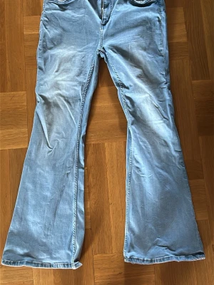Ljusblå utsvängda jeans - Säljer ett par ljusblå jeans med utsvängda ben och klassiska femficksdetaljer. Jeansen har en avslappnad passform och är tillverkade i denim. Perfekta för en retroinspirerad look.