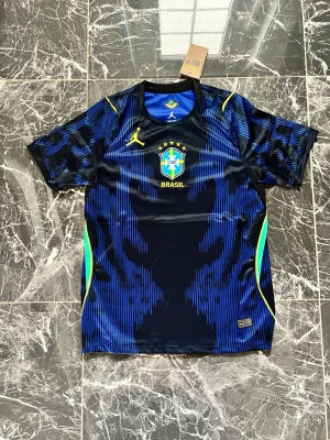 Blå Brasilien 2026 borta vm fotbollströja  - Snygg blå och svart fotbollströja från Nike med Brasilien CBF-logga och gula detaljer. Tröjan har korta ärmar, rund hals och är tillverkad i ett lätt, snabbtorkande material. Perfekt för träning eller match.