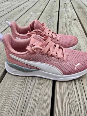 Rosa sneakers från Puma - Snygga rosa sneakers från Puma med vit sula och vit logga på sidan. Ovandelen är i meshmaterial för bra andningsförmåga och skon har klassisk låg profil. Perfekta för en sportig och trendig look.