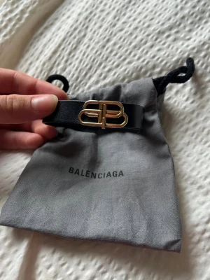 Balenciaga svart läderarmband - Snyggt svart armband i läder från Balenciaga med guldfärgat BB-spänne framtill. Kommer med original dustbag. Perfekt accessoar för dig som gillar stilrena och exklusiva detaljer. Nypris 2700 