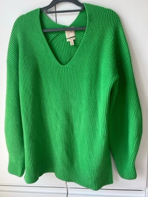 Grön stickad oversized tröja från H&M - Snygg grön stickad tröja från H&M i ullblandning. Tröjan har djup V-ringning, ribbstickad struktur och långa ärmar. Perfekt för dig som vill ha en färgklick i garderoben och gillar oversized känsla.