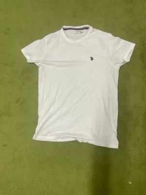 Vit t-shirt från U.S. Polo  - Klassisk vit t-shirt från U.S. Polo Assn. med rund halsringning och liten broderad logga på bröstet. Enkel och stilren design som passar till det mesta. Tillverkad i mjuk bomull för en skön känsla.