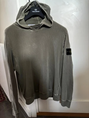 Olivgrön hoodie från Stone Island medium - Säljer en olivgrön hoodie från Stone Island med klassisk patch på vänster ärm. Hoodien har en avslappnad passform, ribbade muddar och är tillverkad i mjuk bomull. Perfekt för dig som gillar streetwear och vill ha en stilren look. I gott skick. Storlek meddium.