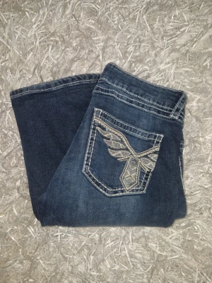 Mörkblå jeans med broderad ficka - Snygga mörkblå jeans med unik broderad bakficka och vita sömmar, de är bootcut o low waist! gina young storlek 170! de är lite slitna nertill men de är ej ngt märkvärdigt 