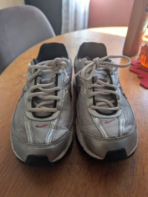 Nike silverfärgade sneakers nypris 999 - Snygga sneakers från Nike i silver och vitt med svarta och röda detaljer. Skorna har klassisk låg modell, mesh- och syntetmaterial samt tydlig Nike-logga på sidan. Perfekta för en sportig och trendig look.